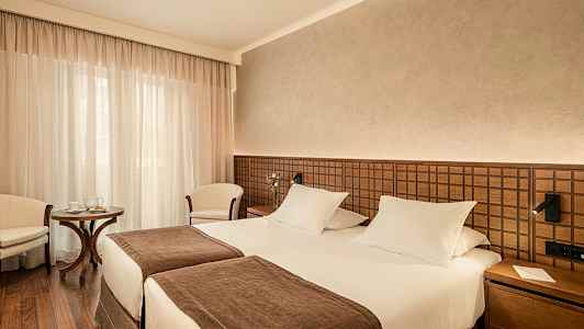 Hotellihuone, jossa on kaksi erillistä vuodetta, ruskea sisustus ja pieni istuinryhmä. (Tekoälyn luoma teksti)