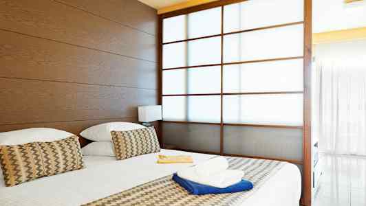 Hotellihuone, jossa on suuri sänky, puupaneelit ja osittain läpinäkyvä liukuovi. (Tekoälyn luoma teksti)