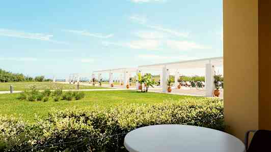 Näkymä terassilta, pyöreä pöytä etualalla, nurmikko ja pergola taustalla. (Tekoälyn luoma teksti)