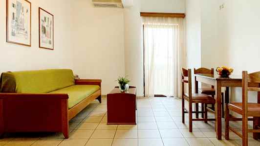 Olohuone, jossa on sohva, sohvapöytä ja ruokapöytä tuoleineen. Vaaleat seinät ja verhot. (Tekoälyn luoma teksti)