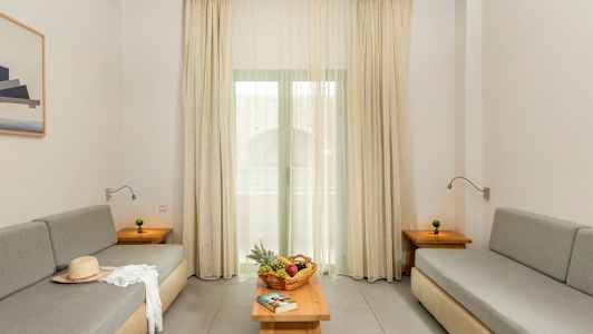 Olohuone, jossa on kaksi harmaata sohvaa, pöytä hedelmäkorilla ja kirjalla sekä verhot ikkunan edessä. (Tekoälyn luoma teksti)