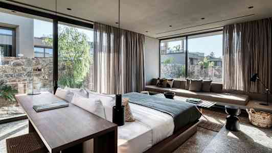 Kuva modernista hotellihuoneesta, jossa on suuri sänky, työpöytä ja sohva, sekä ikkunat, joista näkyy vehreälle sisäpihalle. (Tekoälyn luoma teksti)