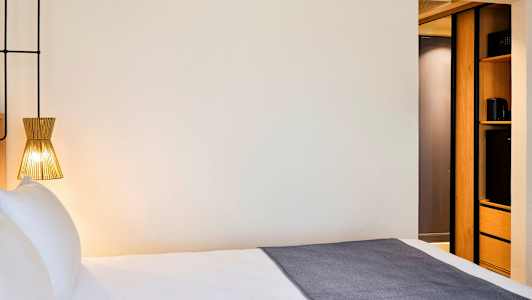 Hotellihuone, jossa on sänky, nykyaikainen lamppu ja osa sisustuksesta säilytystilalla. (Tekoälyn luoma teksti)