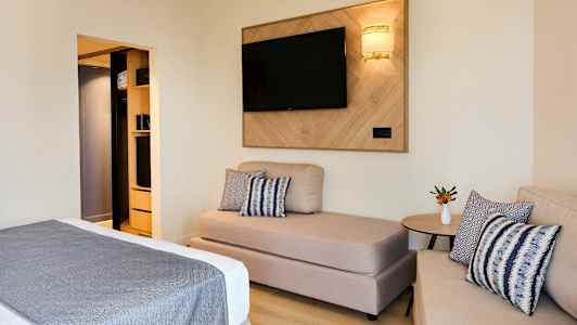 Hotellihuone, jossa sohva, sänky ja TV seinällä. (Tekoälyn luoma teksti)