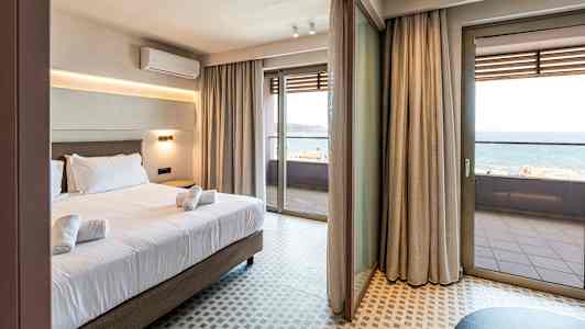 Hotellihuone, jossa sänky ja pyyhkeet. Suuret lasiovet johtavat parvekkeelle, jolta näkyy meri. (Tekoälyn luoma teksti)