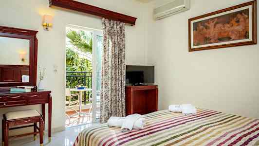 Hotellihuone, jossa on sänky, televisio, meikkipöytä ja parveke näkymällä palmupuun suuntaan. (Tekoälyn luoma teksti)