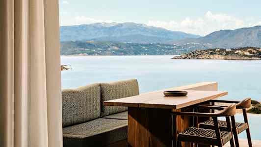 Näkymä puupöydästä ja tuoleista, taustalla meri ja vuoria. (Tekoälyn luoma teksti)