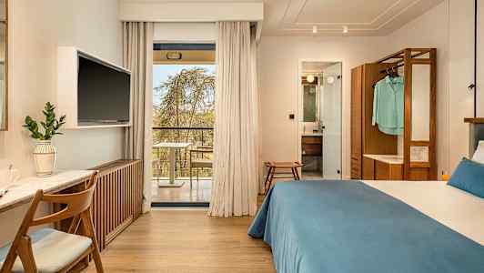 Hotellihuone, jossa on parivuode, työpöytä ja televisio. Lasiovet johtavat parvekkeelle. Kylpyhuone näkyy avoimen oven läpi. (Tekoälyn luoma teksti)