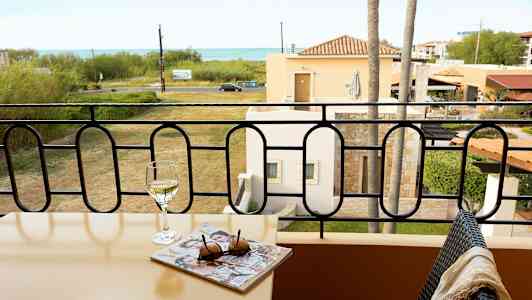 Parveke, jossa pöytä, viinilasi ja lehti, näkymä nurmikolle ja merelle. (Tekoälyn luoma teksti)