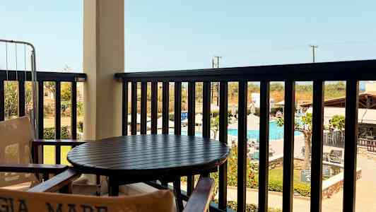 Näkymä parvekkeelta, jossa on pöytä ja tuolit, sekä uima-allas ja ympäröivät rakennukset taustalla. (Tekoälyn luoma teksti)