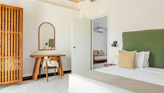 Makuuhuone, jossa on vihreä sängynpääty, puinen kirjoituspöytä ja peili sekä puinen vaatekaappi. (Tekoälyn luoma teksti)