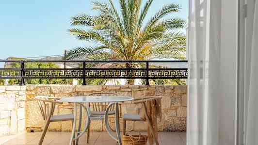 Näkymä aurinkoiselle terassille, jossa pöytä ja tuolit, palmupuun ja sinisen taivaan suuntaan. (Tekoälyn luoma teksti)