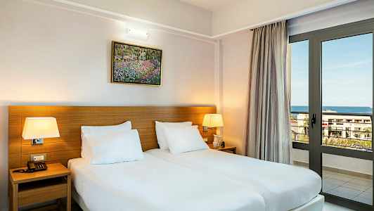 Huone, jossa on kaksi erillistä vuodetta, pöytävalaisimia ja ikkunaoovi, joka avautuu merelle. (Tekoälyn luoma teksti)