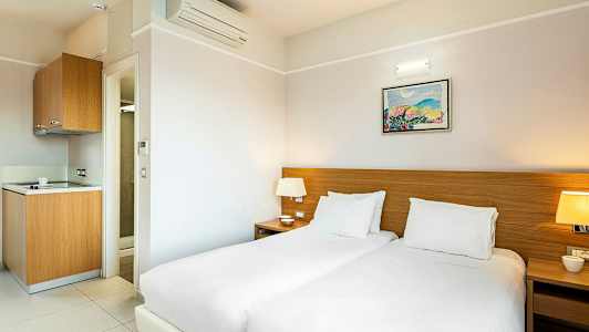 Hotellihuone, jossa kaksi vuodetta, yöpöytä ja pieni keittokomero. (Tekoälyn luoma teksti)