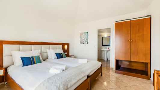 Hotellihuone, jossa on kaksi pedattua sänkyä, vaatekaappi ja kylpyhuoneen sisäänkäynti. (Tekoälyn luoma teksti)