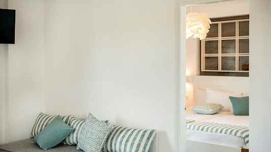 Hotellihuone, jossa etualalla sohva tyynyineen ja taustalla pedattu sänky. (Tekoälyn luoma teksti)