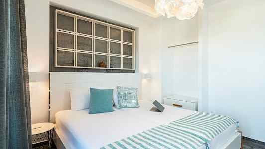 Vaalea ja moderni hotellihuone, jossa parivuode, lukuvalot, valkoiset seinät ja koristeellisia yksityiskohtia. (Tekoälyn luoma teksti)