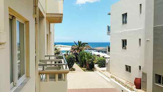 Rakennukset parvekkeineen avautuvat palmujen reunustamalle kävelytielle, taustalla meri. (Tekoälyn luoma teksti)