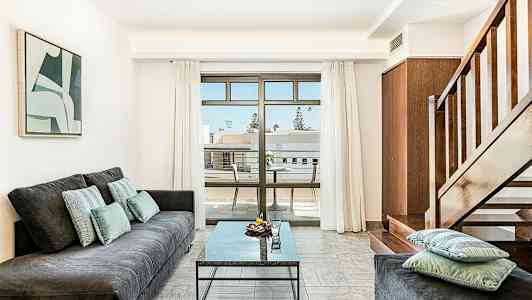 Olohuone, jossa sohva, pöytä ja portaat sekä parveke näköalalla. (Tekoälyn luoma teksti)