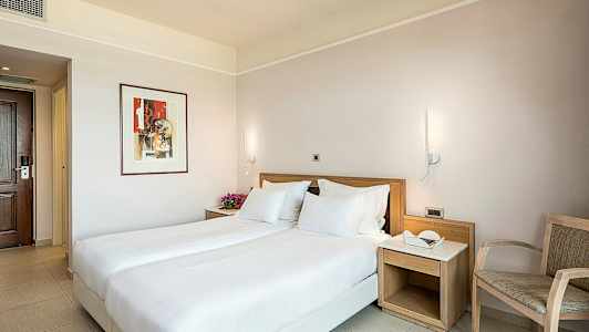 Hotellihuone, jossa on parivuode, yöpöytä ja tuoli. (Tekoälyn luoma teksti)