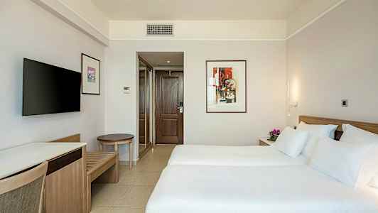 Hotellihuone, jossa kaksi yhden hengen sänkyä, koristeellinen taide seinällä ja televisio. (Tekoälyn luoma teksti)