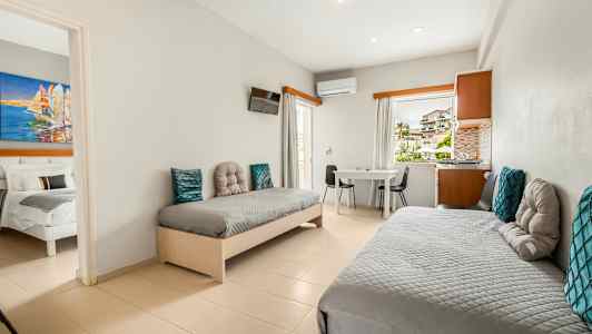 Hotellihuone, jossa kaksi yhden hengen vuodetta, pöytä ja tuolit, sekä näkymä ikkunan läpi. (Tekoälyn luoma teksti)