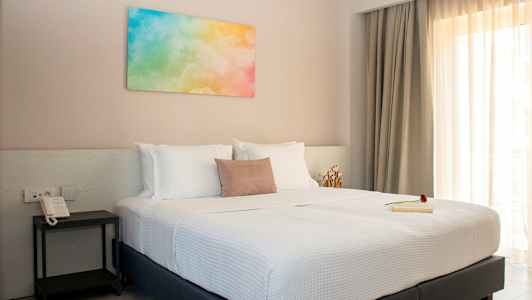 Makuuhuone, jossa parivuode, valkoiset vuodevaatteet ja värikäs maalaus seinällä. (Tekoälyn luoma teksti)