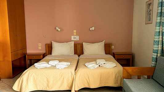 Hotellihuone, jossa on kaksi yhden hengen vuodetta, yöpöydät ja taitellut pyyhkeet vuoteilla. (Tekoälyn luoma teksti)