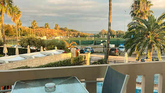 Näkymä terassilta urheilukentälle, jota ympäröivät palmut ja pysäköintialue. (Tekoälyn luoma teksti)