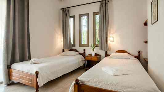 Huone, jossa kaksi erillistä vuodetta, yöpöytä välissä, valkoiset vuodevaatteet ja harmaat verhot ikkunan edessä. (Tekoälyn luoma teksti)