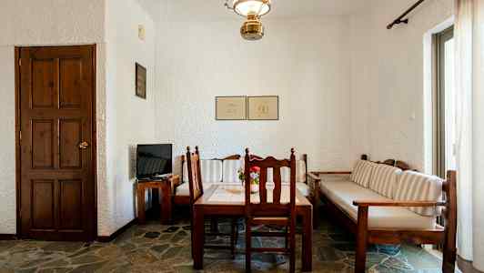 Huone, jossa on puupöytä ja tuolit, sohva sekä ovi ja televisio puisella pöydällä. (Tekoälyn luoma teksti)