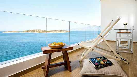 Näkymä parvekkeelta, jolla on tuoleja, pöytä ja kulhollinen hedelmiä puurahiolla, taustalla meri ja saaria. (Tekoälyn luoma teksti)