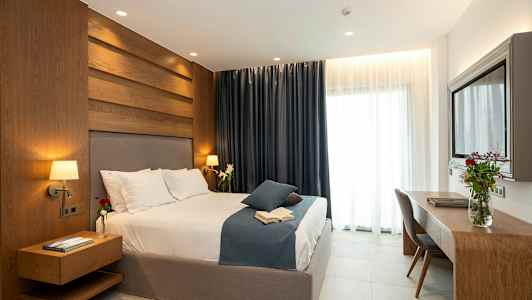 Nykyaikainen makuuhuone, jossa on iso sänky, puupaneeli, tummat verhot ja kirjoituspöytä, jolla on kukkamaljakko. (Tekoälyn luoma teksti)