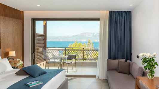 Hotellihuone, jossa sänky, sohva, kirjoituspöytä ja parvekkeen näkymä merelle. (Tekoälyn luoma teksti)