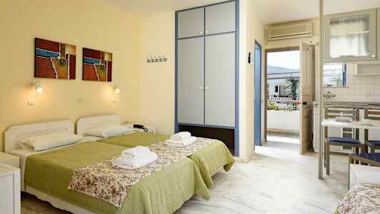 Kaksi vuodetta vihreillä peitteillä ja kukkakuvioisilla päiväpeitteillä huoneessa, jossa on kaappi, ruokapöytä ja parvekkeen ovi. (Tekoälyn luoma teksti)