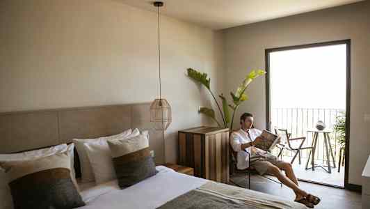 Hotellihuone, jossa on pedattu parisänky, moderni sisustus ja parveke ulkokalusteilla ja vihreällä kasvillisuudella. (Tekoälyn luoma teksti)