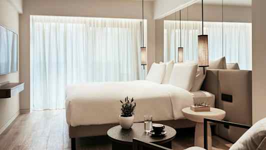 Moderni hotellihuone, jossa on iso sänky, valkoiset lakanat ja minimalistinen sisustus. (Tekoälyn luoma teksti)