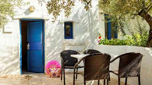 Valkoinen rakennus, sininen ovi ja ikkunat, pöytä ja tuolit terassilla. (Tekoälyn luoma teksti)