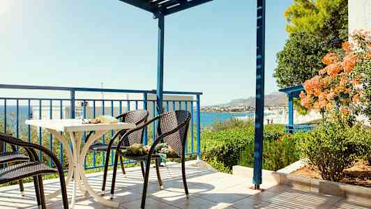 Terassi, jossa tuoleja ja pöytä, merinäköala ja vehreä ympäristö. (Tekoälyn luoma teksti)