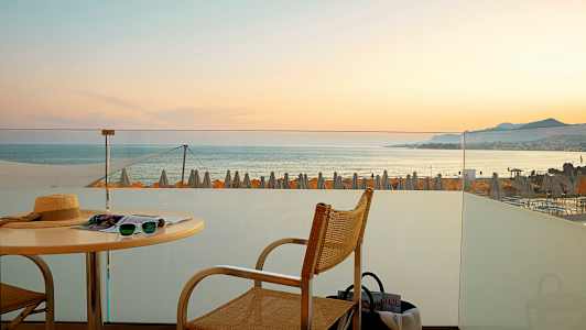 Näköala terassilta merelle, taustalla auringonlasku ja rantavarjot. (Tekoälyn luoma teksti)