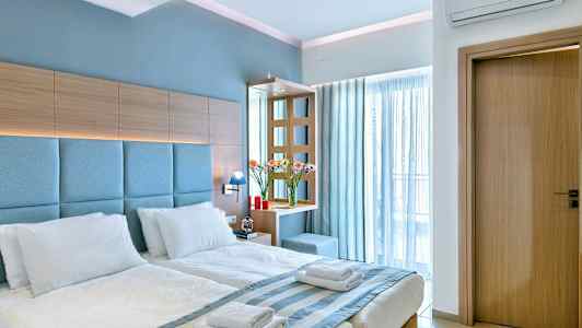 Hotellihuone, jossa on parivuode, valkoiset vuodevaatteet, puupaneelia ja sinisiä yksityiskohtia. (Tekoälyn luoma teksti)