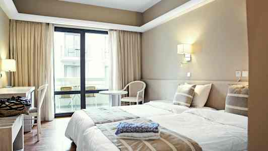 Hotellihuone kahdella yhden hengen sängyllä, työpöydällä ja parvekkeella. (Tekoälyn luoma teksti)