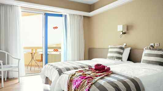 Hotellihuone, jossa on kaksi erillistä vuodetta, raidalliset vuodevaatteet ja ovi parvekkeelle. (Tekoälyn luoma teksti)