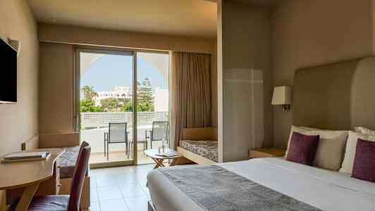 Moderni hotellihuone, jossa on parivuode, työpöytä, istuinkalusteet ja suuri ikkuna, joka johtaa parvekkeelle näkymällä puutarhaan. (Tekoälyn luoma teksti)