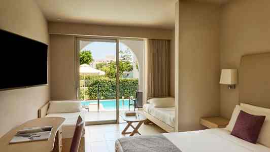 Hotellihuone, jossa on parivuode, kirjoituspaikka ja lisävuode. Ulkona näkyy terassi ja uima-allas. (Tekoälyn luoma teksti)