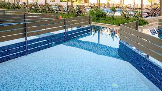 Kuvassa nykyaikainen uima-allas, jossa on sinistä mosaiikkia ja puuaidan. (Tekoälyn luoma teksti)