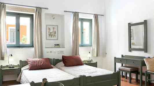 Valokuva vaaleasta makuuhuoneesta, jossa on kaksi erillistä vuodetta, ikkunat valon sisääntulolla ja puukalusteet. (Tekoälyn luoma teksti)