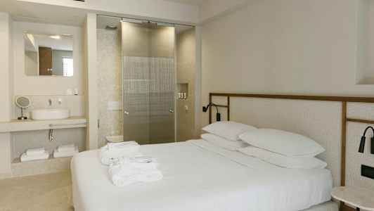 Modernisti sisustettu hotellihuone, jossa parivuode, pesuallas ja lasiovi kylpyhuoneeseen. (Tekoälyn luoma teksti)