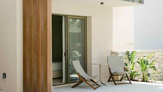 Terassi, jossa on kaksi tuolia, pieni pöytä ja vihreitä kasveja lasioven vieressä. (Tekoälyn luoma teksti)