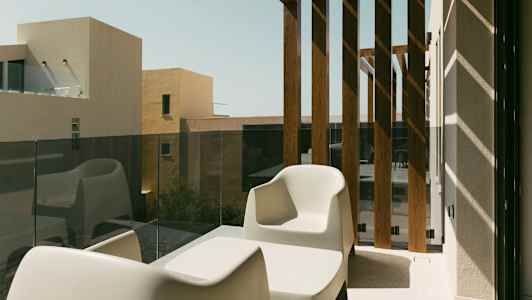 Kaksi valkoista tuolia ja pöytä parvekkeella, jossa on lasikaide ja puupaneelit. (Tekoälyn luoma teksti)